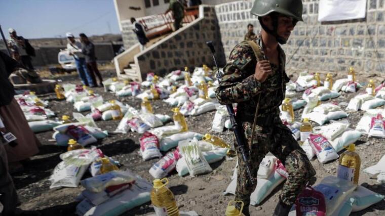 A Houthi-affiliated soldier walks among humanitarian aid supplies in a displaced persons camp